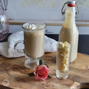 White Chocolate Mocha Latte with whipped cream. A bottle of white chocolate syrup, white chocolate chips, and a rose in the picture.