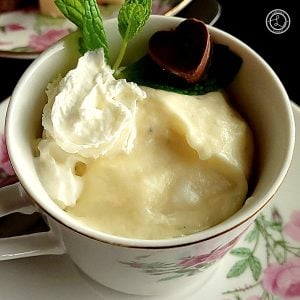 White Chocolate Mousse a close up photo. Mousse in a teacup with whipped coconut cream, sprig of mint, and small piece of chocolate.