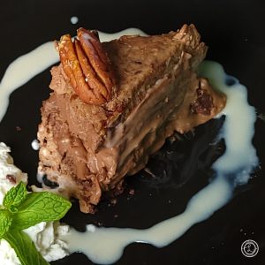 Thin vanilla sauce around a slice of Gluten-Free German Chocolate Cheesecake