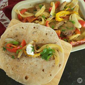 Gluten-Free Steak Fajitas on a tortillas with the meat and vegetables behind it.