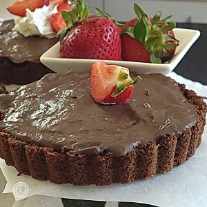 Gluten-Free Chocolate Tarts with a quarter of a piece of fresh strawberry on top. Strawberries and another tart in the background.