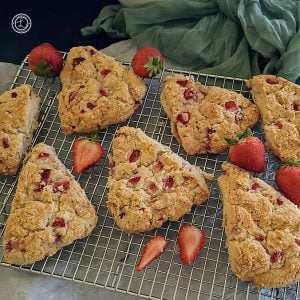 Gluten-Free Strawberry Scones Recipe on a cooling rack with some strawberries whole and sliced. A napkin in the background.