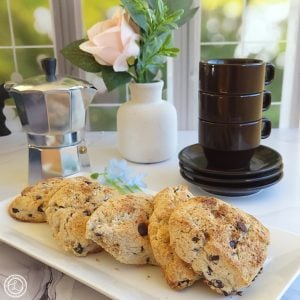 A platter of scones with espresso cups, an espresso coffeepot, and flowers in a vase.