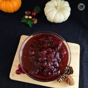 Refined Sugar-Free Cranberry Sauce a bowl of it on top of a small cutting board, Mini pumpkins in the background.