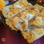 Three filled Gluten-Free Gingersnap crepes on a plate with one bite on a fork. Topped with whipped cream and orange strips.