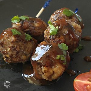 Sweet and Sour Meatballs: A close up of 5 meatballs on a plate with a slice of tomato in the corner.