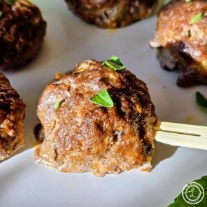 Gluten-Free Buffalo Meatballs a close up of a meatball on a wooden serving fork.